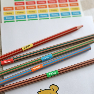 Lápis de cor com ministickers com o nome Finley, ao lado de uma cartela de etiquetas