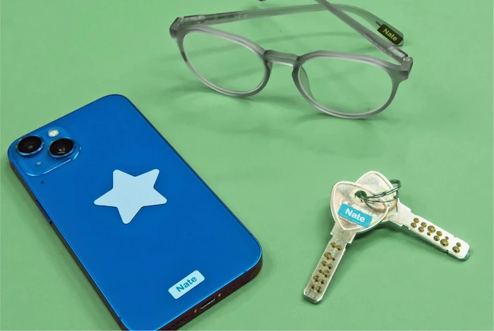 Celular azul, óculos e chaves com ministickers com o nome Nate